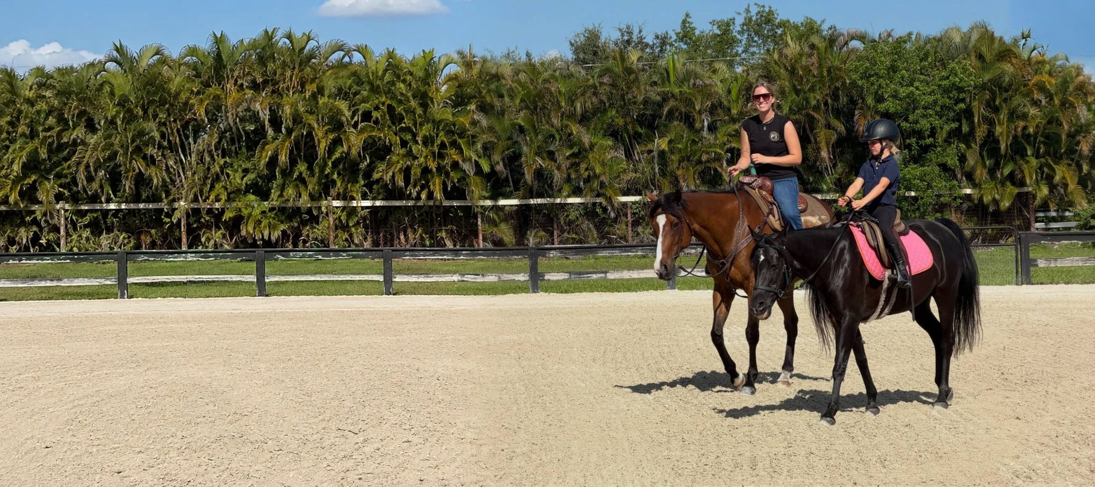 Stella riding Western beside a young rider on a black horse in the arena