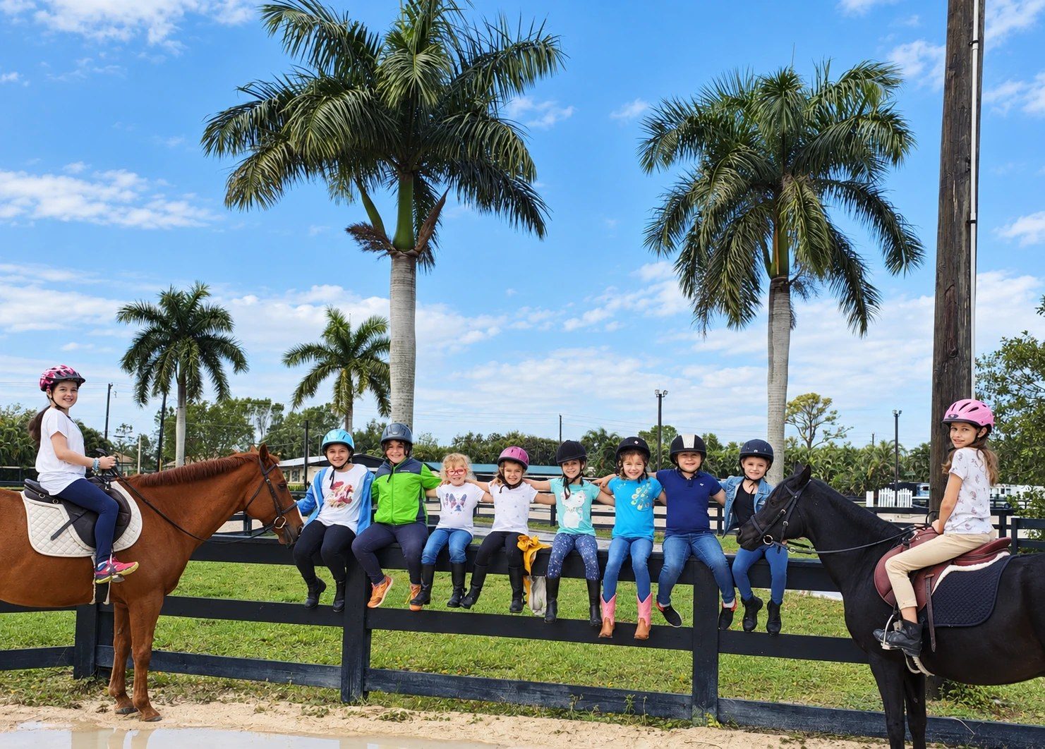 Campers sitting on the arena fence under the palms between two riders