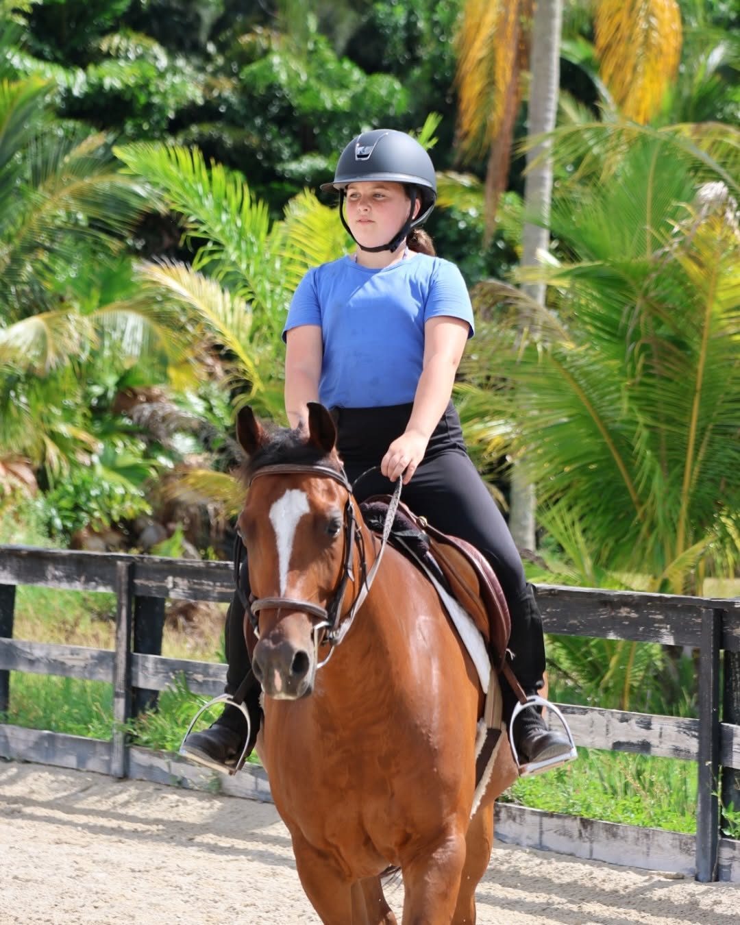 A rider in a blue shirt on a chestnut horse with a white blaze