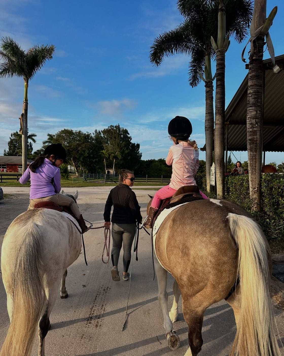 An instructor leading two young riders under the palms