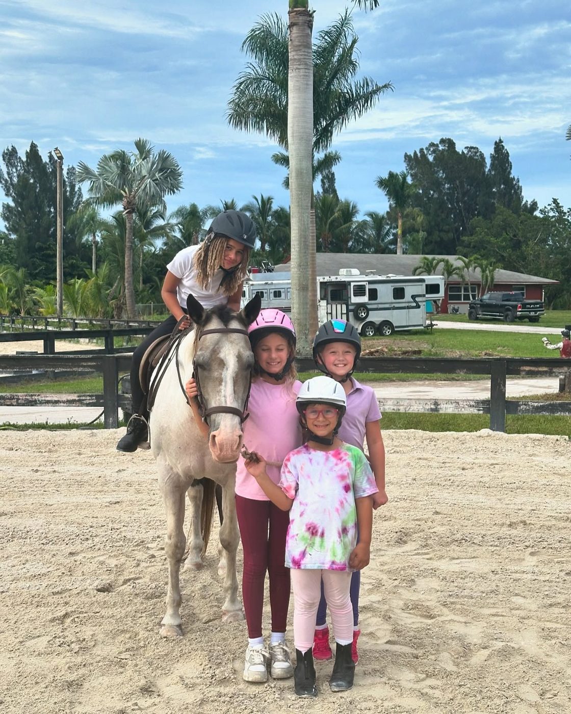 Four smiling campers in helmets with a gray pony in the arena