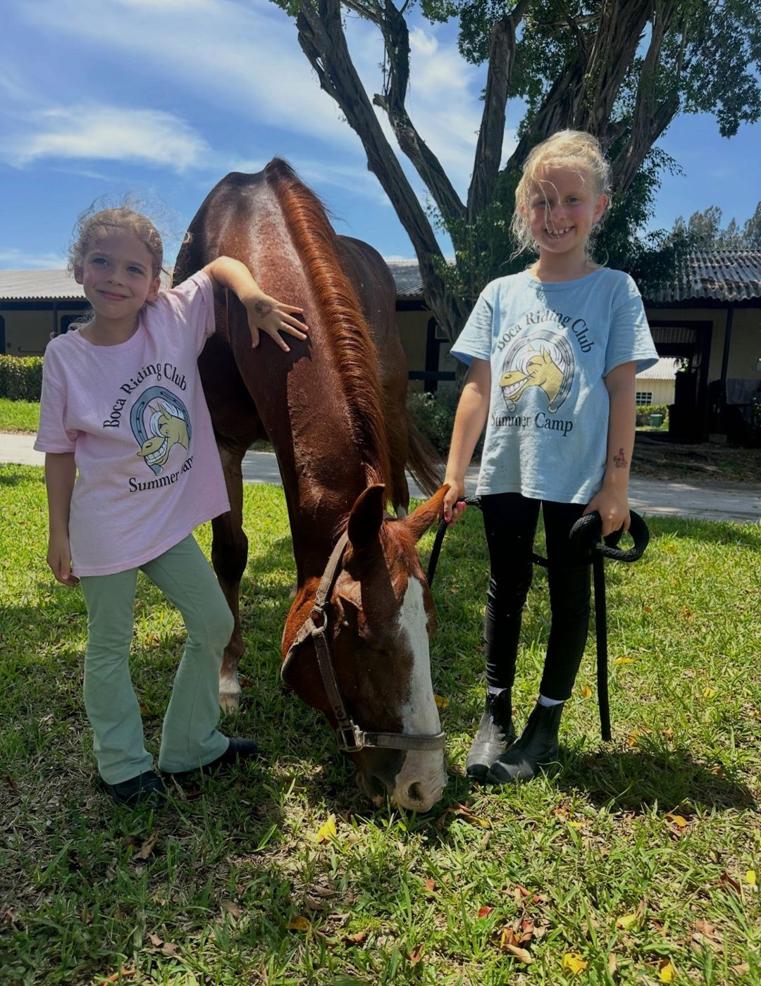 Two campers in Boca Riding Club summer camp shirts with a grazing chestnut