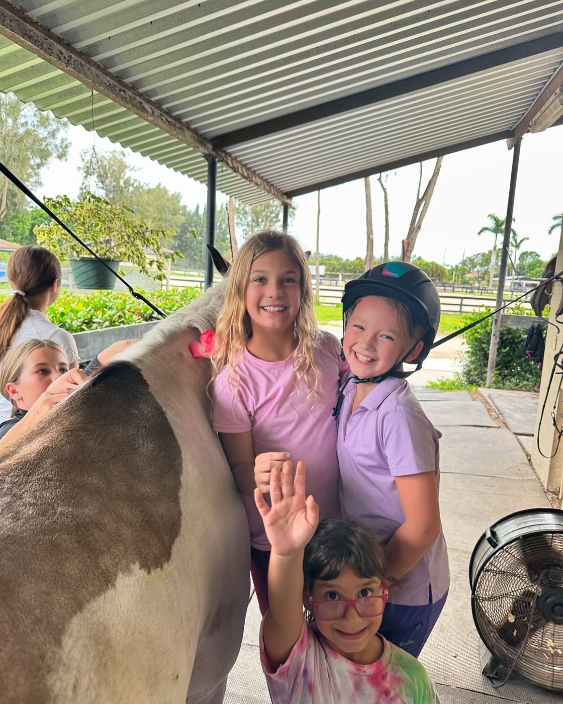 Campers waving next to a paint horse in the barn